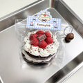 Strawberry chocolate cake taba squishy in a clear zip pouch with a blue gingham label and brown bell charm